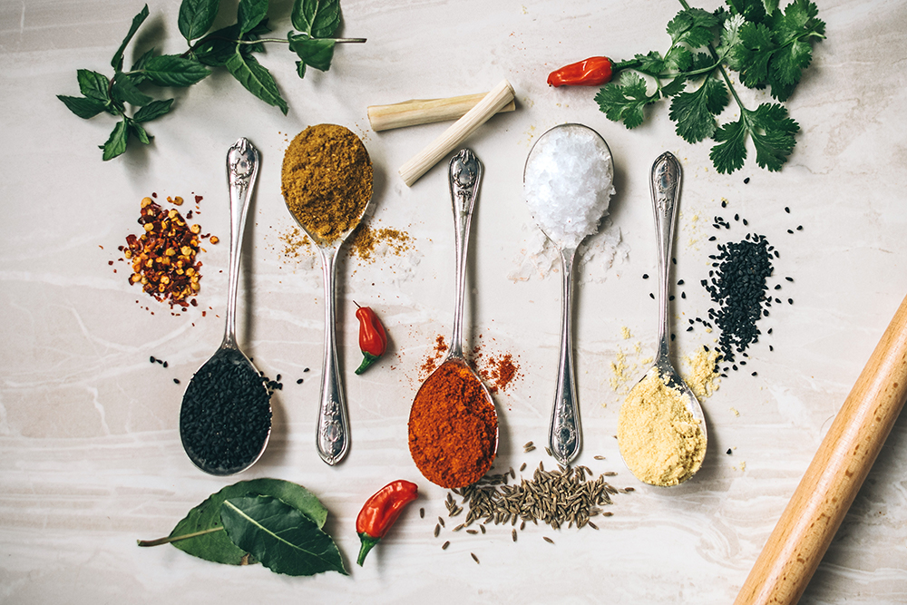 Colorful spices and herbs arranged on silver spoons against a rustic wooden background